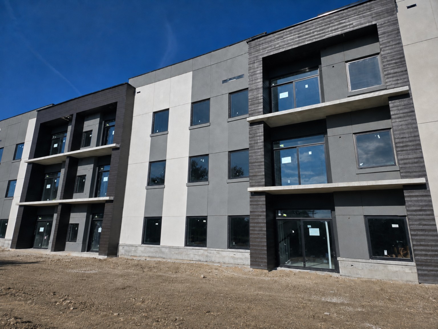 Three-story multifamily building with gray and white EIFS panels, dark faux wood accents, and balconies