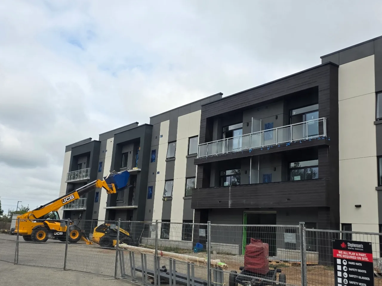 Ladona River Apartments during construction, with StoTherm ci EIFS and dark faux wood going up behind site fencing and a telehandler